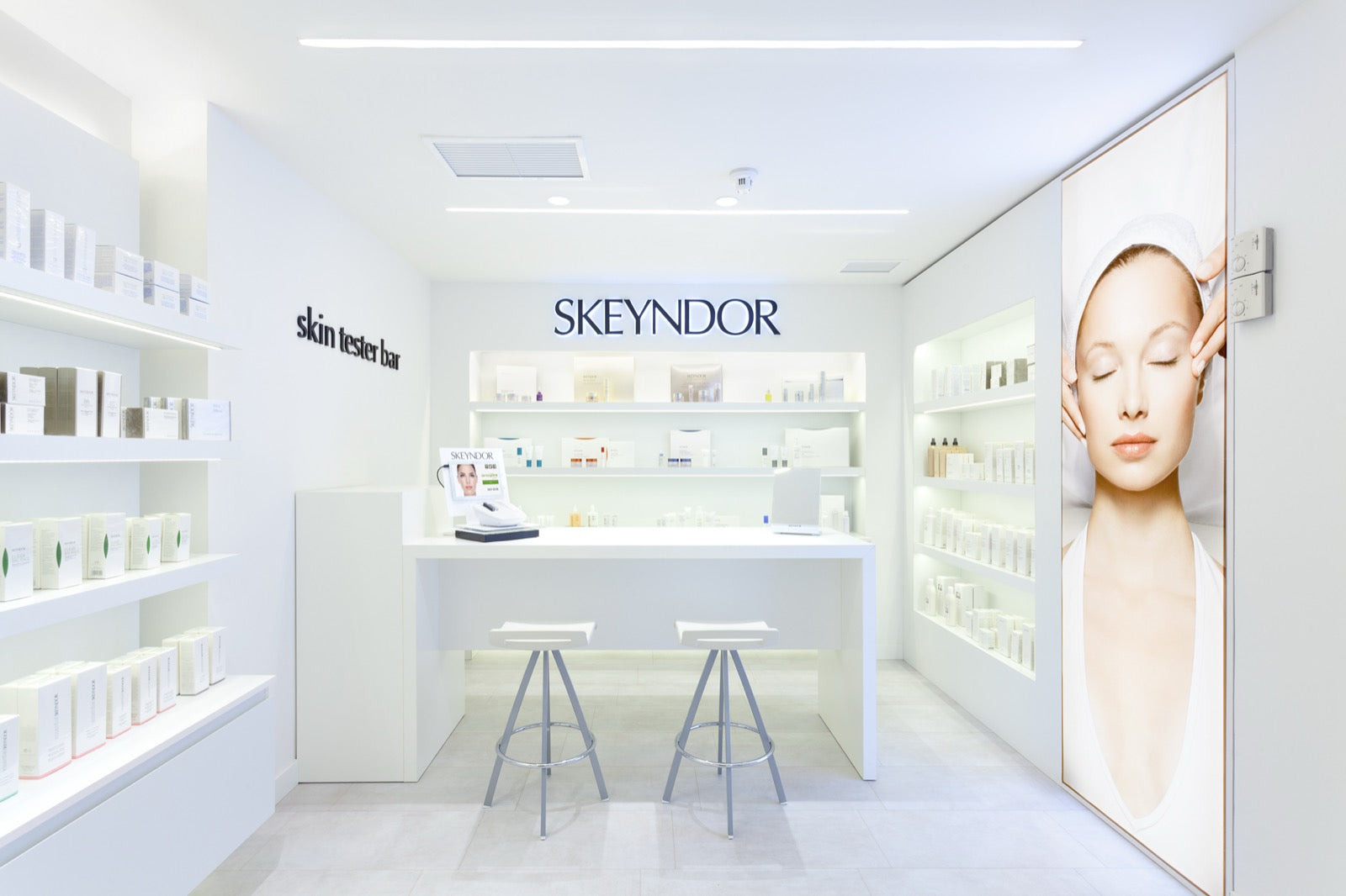 Interior of a genuine SKEYNDOR skin tester bar, white shelving stocked with product beneath the SKEYNDOR logo